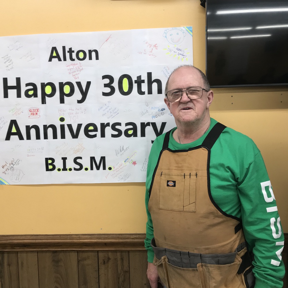 Alton Foskey, wearing a green BISM shirt, standing in front of a sign reading Happy 30th Anniversary