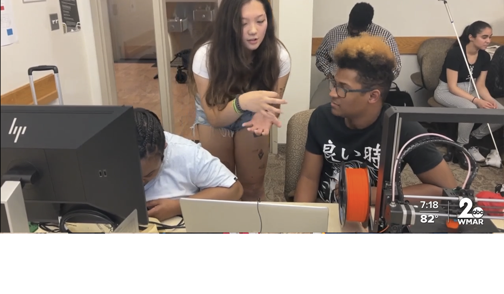 Harford Community College student helps two blind campers 3D print personalized luggage tags in computer lab equipped with 3D printers and computers with printing software. More campters wait their turn.